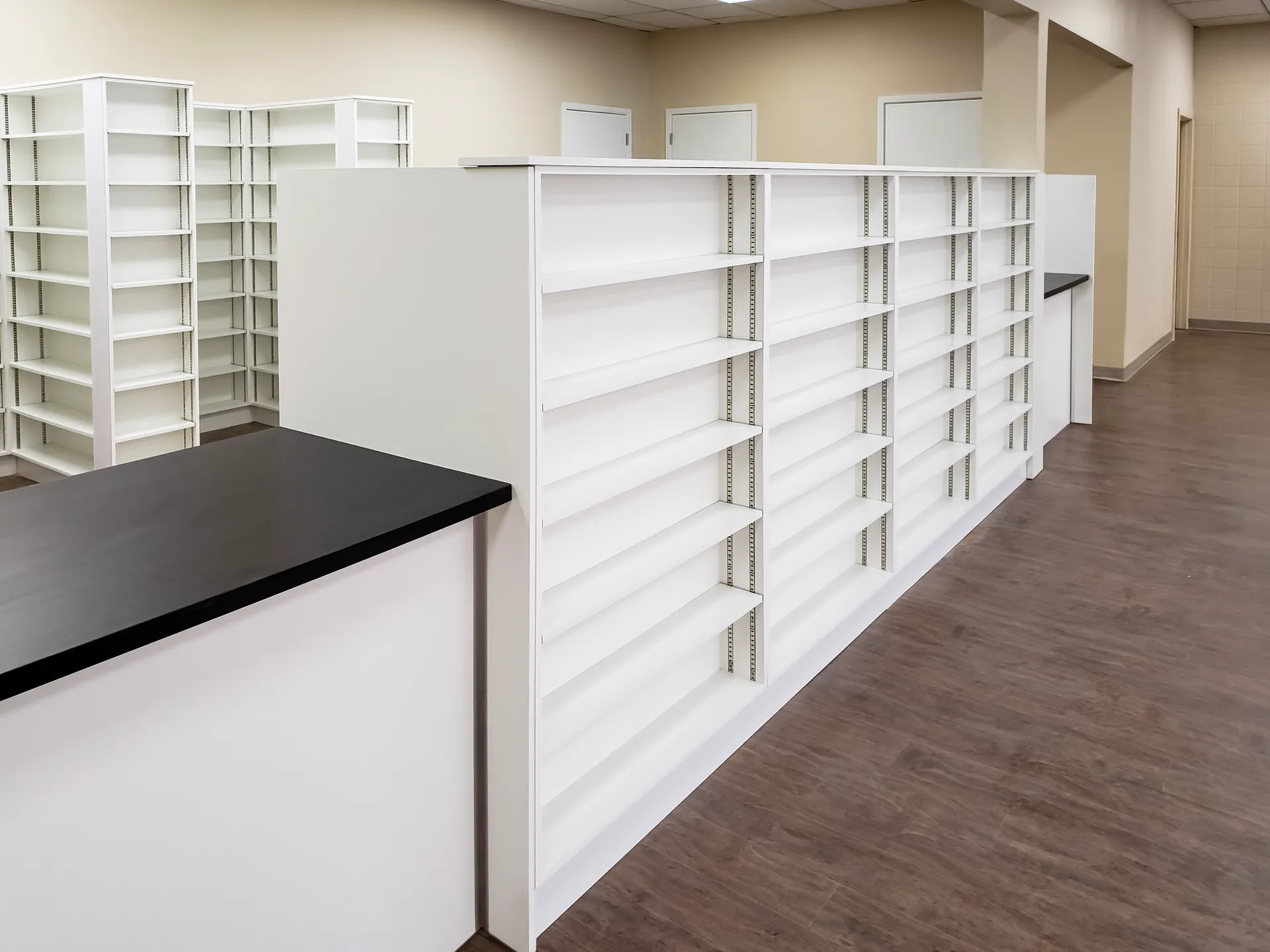 Full height white shelving units and adjustable shelf wall in a pharmacy back of house