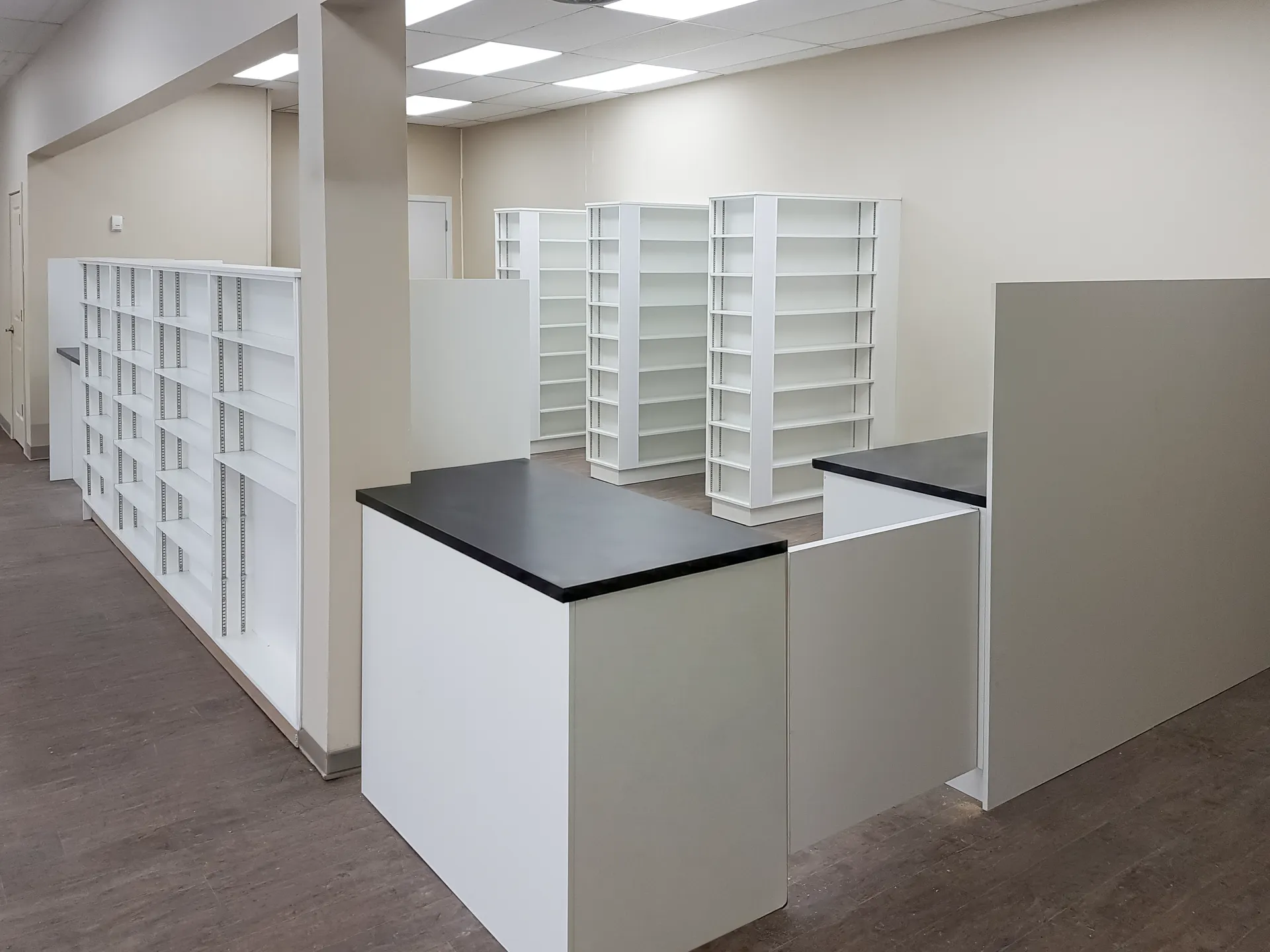 Pharmacy retail floor with white gondola shelving and till counter before stocking